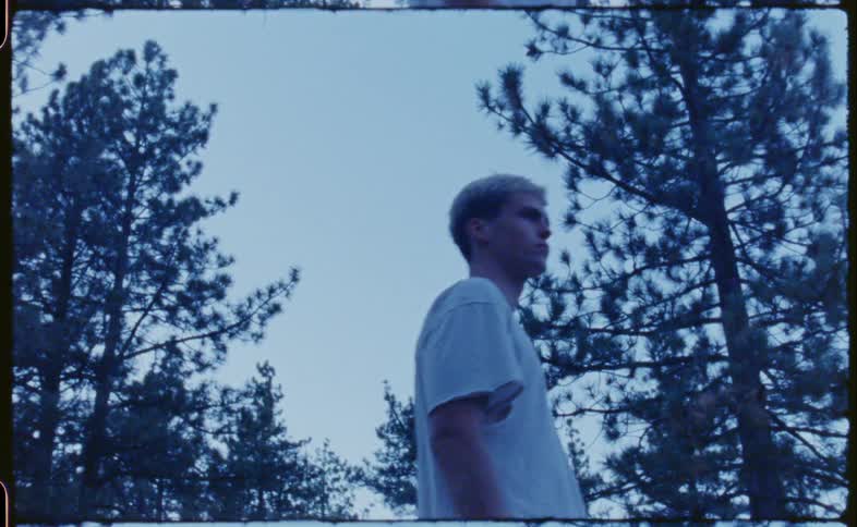 Blonde man with a white shirt walks in the woods