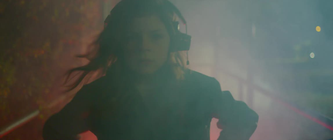 Girl wearing overalls dancing outside a building at night surrounded by white smoke