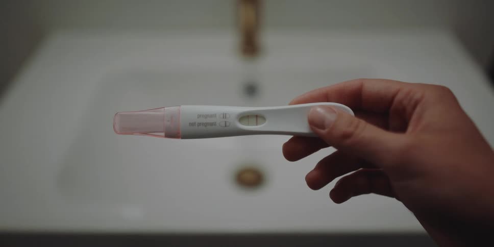 A person in a bathroom looking at a pregnancy test with a sink and faucet in the background