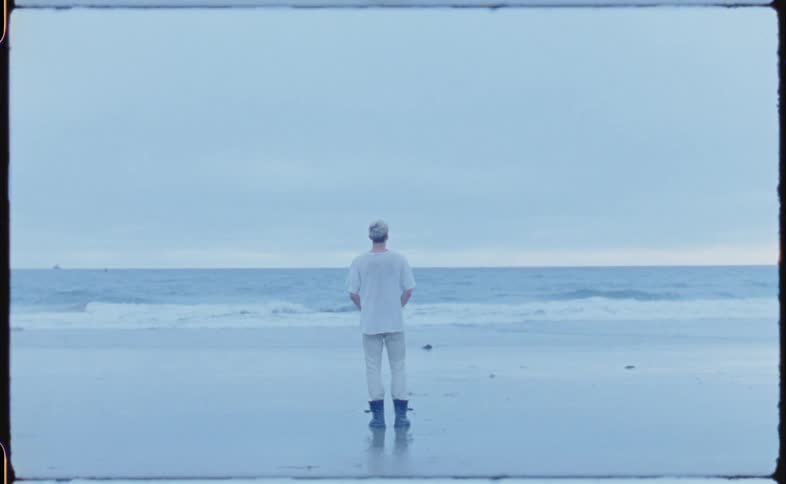 A man wears galoshes as he walks on the beach toward the ocean