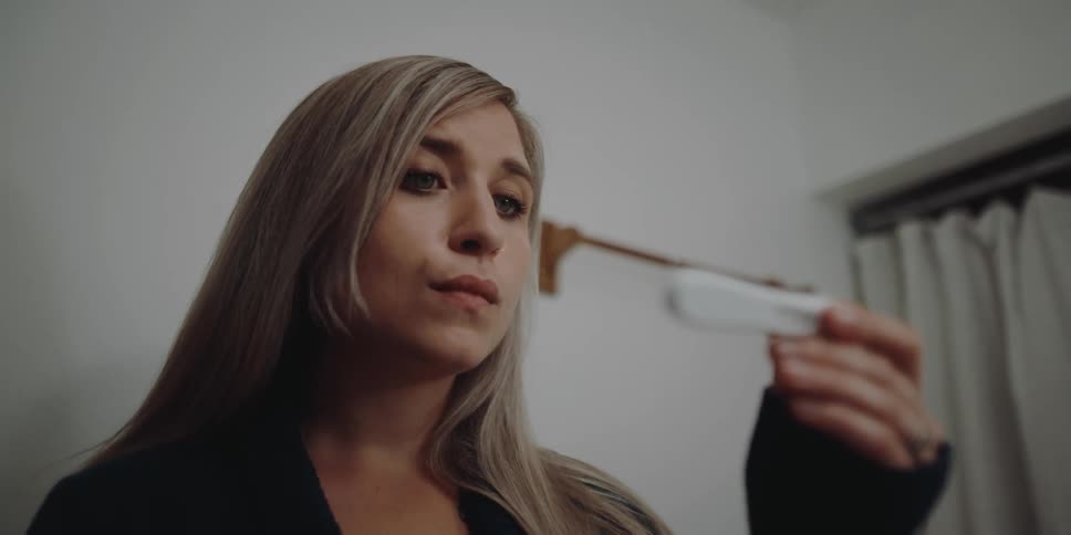 A woman is looking at a pregnancy test in the bathroom