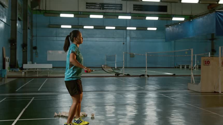 A female practices badminton by herself in a gym