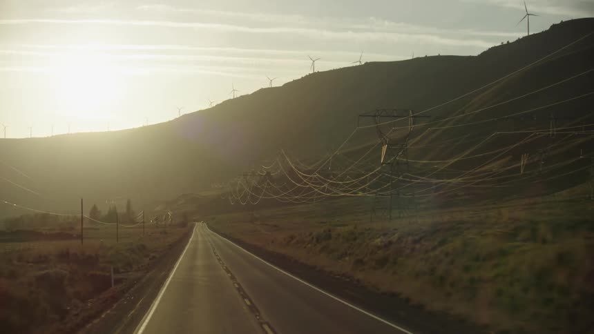Five-hundred kilovolt (500 kV) three-phase high energy transmission lines Bundled 3-ways as seen at sunset with windmills from the perspective of driving down the highway