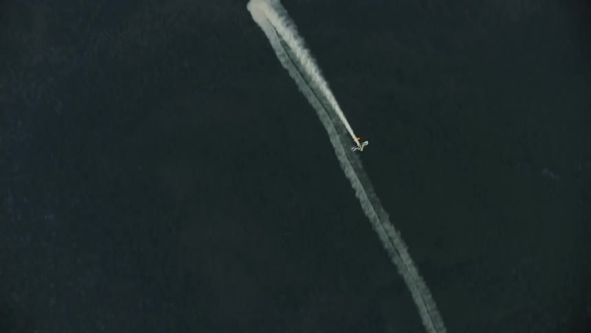 A plane is looping with smoke over the mountains flying directly up at the camera in this dramatic shot