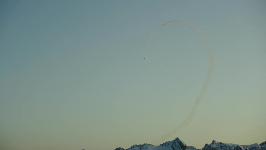 An acrobatic single engine airplane flies huge loops as the sun is setting in the western sky