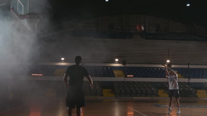 A man passing a basketball to a girl as she shoots the ball into a basketball hoop in a gym