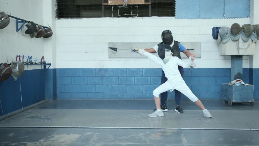 A boy works with his fencing coach on lunging forward