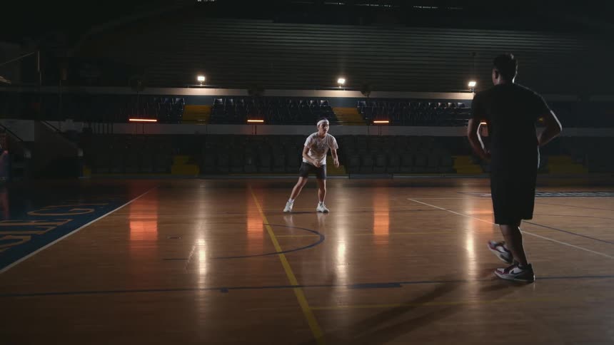 Coach training a basketball player inside a dimly lit indoors court
