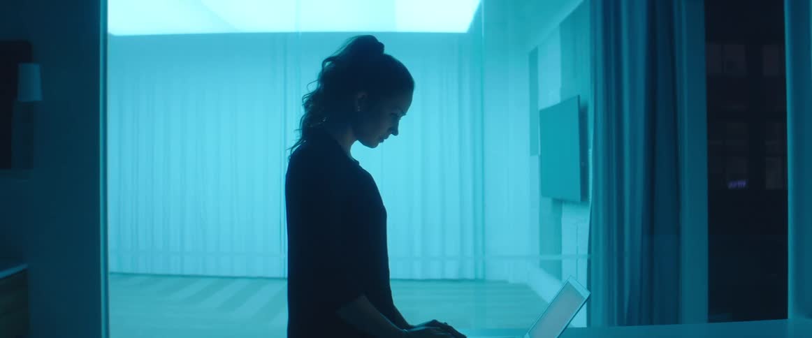 A nurse walks up to a laptop and begins typing in a room with blue lighting