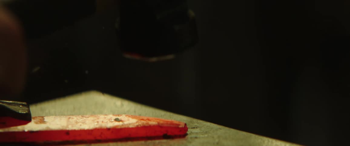 A blacksmith hammering a piece of red hot metal over an anvil inside a dark room