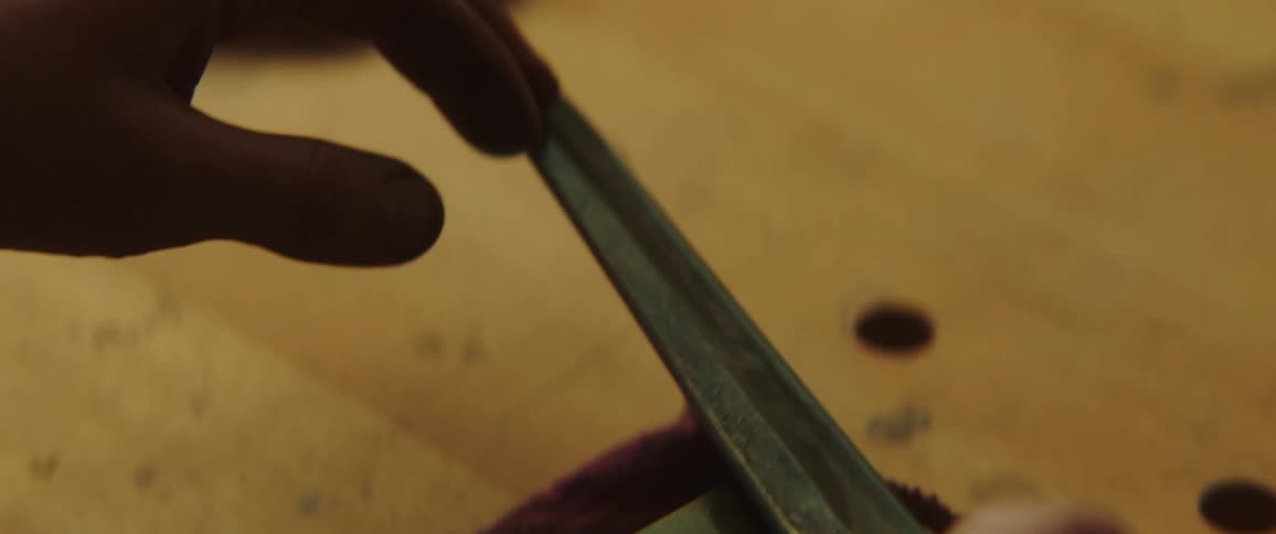 A man sharpens a long blade against a cement block