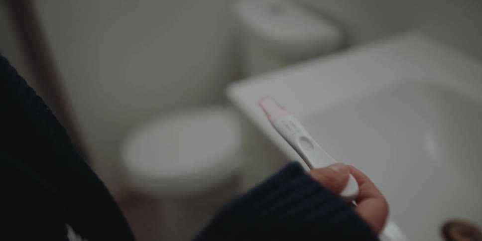 A woman is holding a pregnancy test in the bathroom