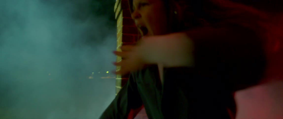 Girl wearing overalls dancing outside a building at night surrounded by white smoke