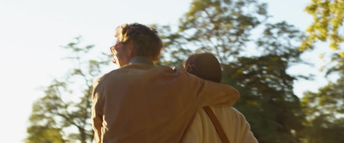 A male and female couple walking together arm and arm near a lake and trees