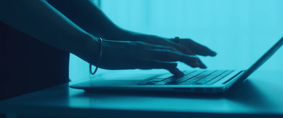 Young person standing in a room under blue lights working on a laptop