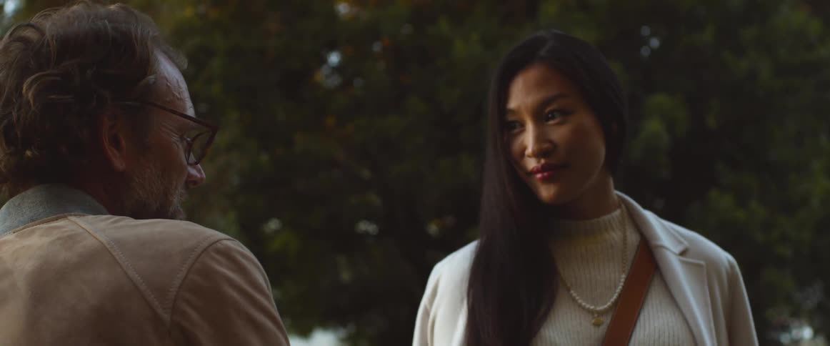 Middle aged man with glasses and brown jacket talks to asian woman with straight hair a white sweater and a topcoat outdoors