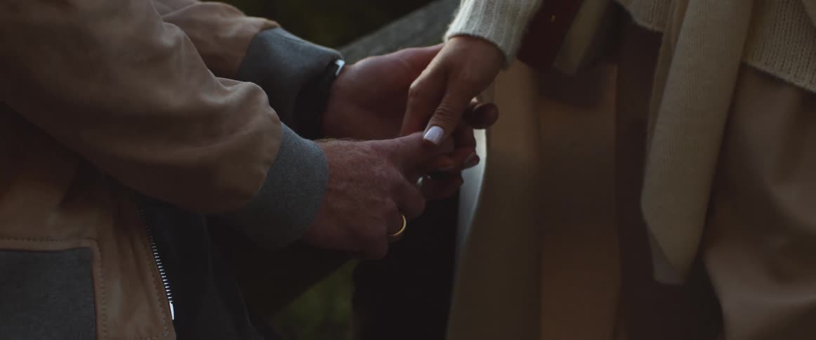 A man and a woman in a bridge holding hands with trees the sky and clouds in the background
