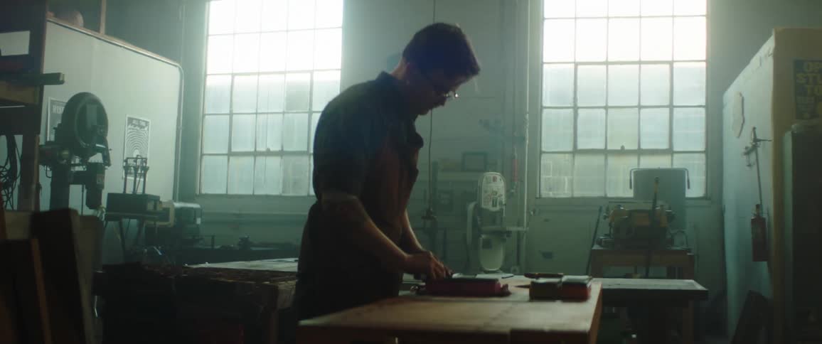 A warehouse employee grabs an knife and takes it over to a table to be sharpened