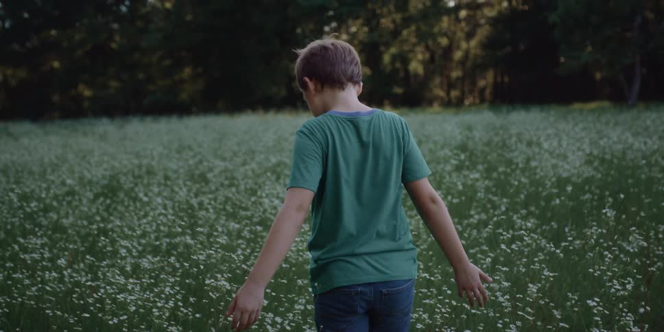 Boy with a green t shirt and shorts walks across the field with flowers