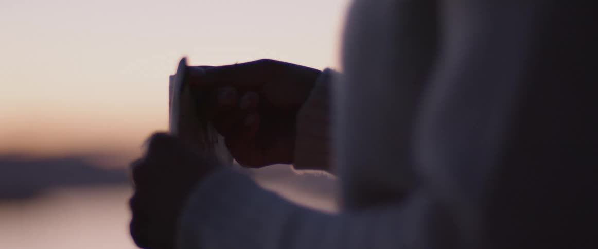 A woman with a sweater opening an envelope with the sky and clouds in the background