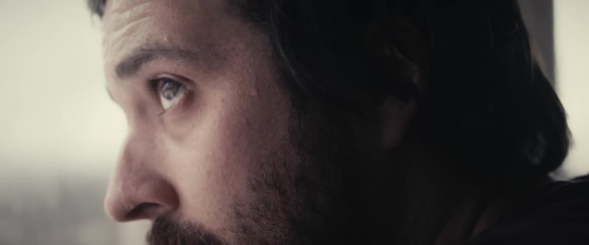A man staring out of a window sweating and looking around nervously