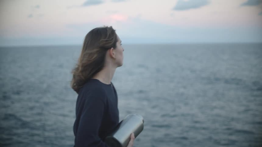 A woman on a beach sprinkling ashes from an urn with the sky and clouds in the background