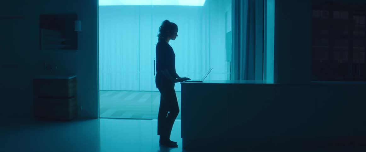A silhouette of a woman in a room typing on a laptop with a wall in the background