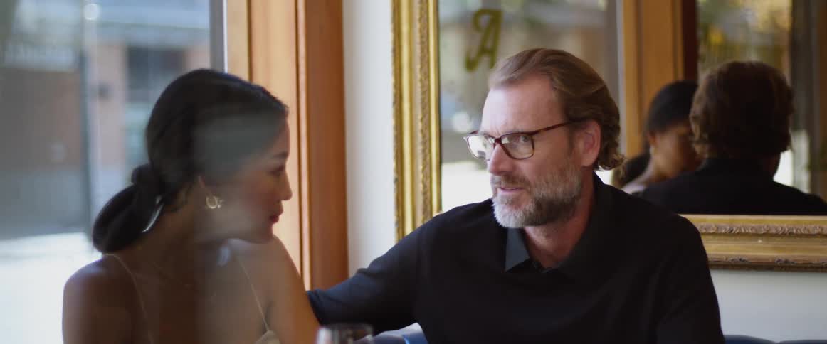 A man and a woman sitting in a restaurant by a table with a window and a mirror in the background