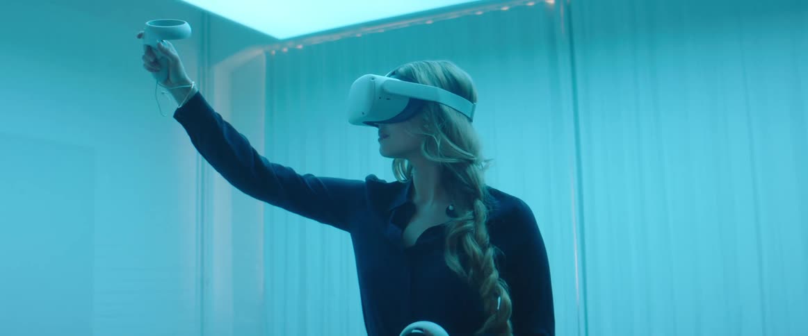 A woman wearing a virtual reality headset holds a controller and waves it around in front of herself