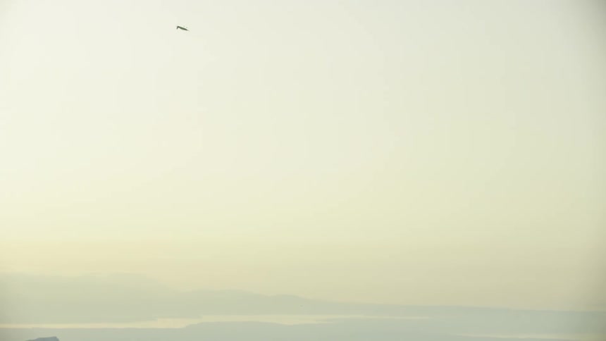 A small single engine piston airplane climbs sharply right in front of a huge jagged mountain peak then climbs straight up into a golden sky