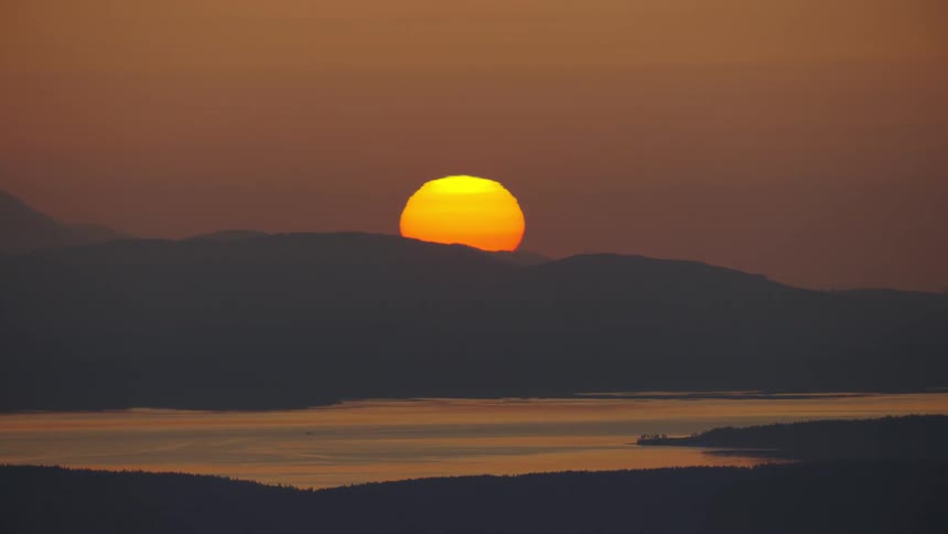 A dramatic winter sun is setting on a tree lined ridge high above the Puget Sound and Pacific Ocean in this radical aerial landscape shot