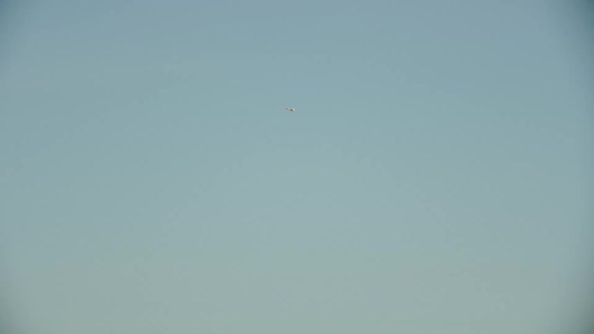 An airplane flying in the air and doing tricks with a mountain range the sky and clouds in the background