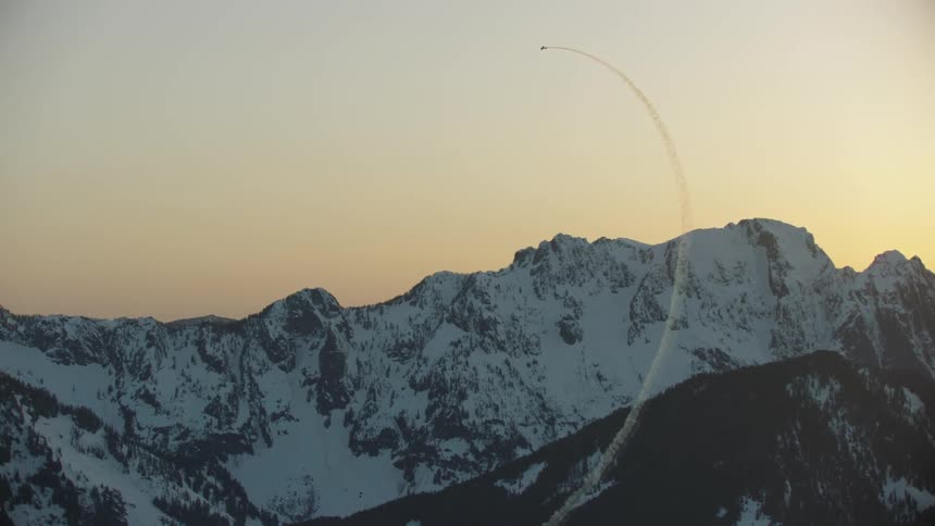An acrobatic airplane flying loops with smoke with a mountain range the sky and clouds in the background at sunset