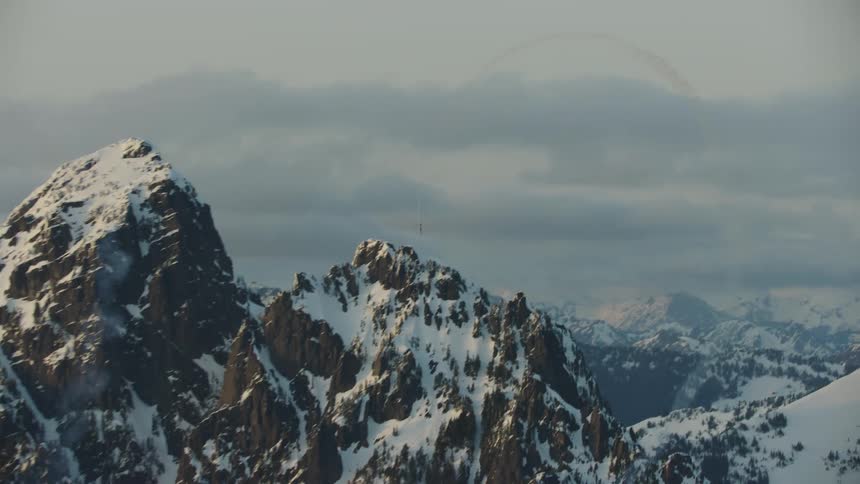 Single engine aircraft doing acrobatic maneuvers over the snow covered peaks of a mountain range in the heart of winter at sunset