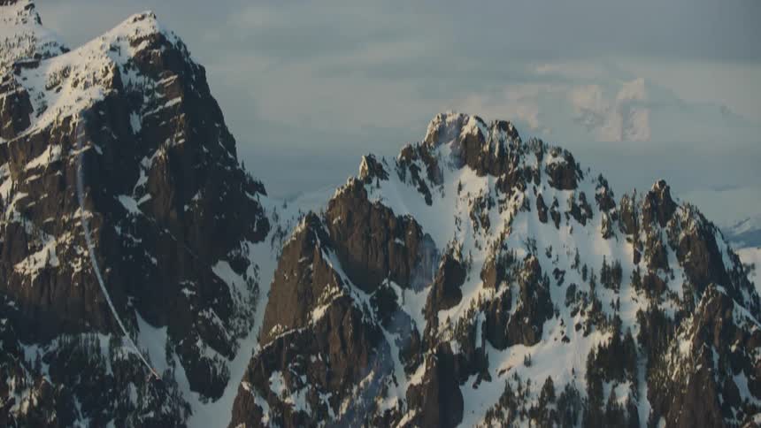 An acrobatic airplane does a loop leaving a trail of smoke in the sky as it flies over snow covered mountains with Mount Rainier in the background