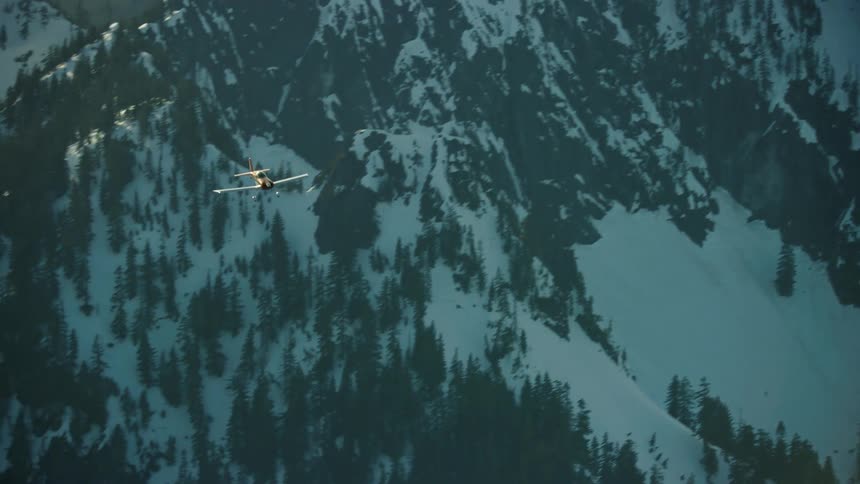 Single engine airplane flying quickly over snow covered mountains in the winter on the way to somewhere cool