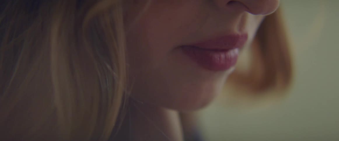 Blonde woman with a nose piercing sits at table and looks down