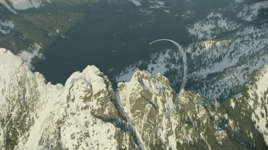 Single engine aircraft doing acrobatic maneuvers over the snow covered peaks of a mountain range in winter evoking excitement