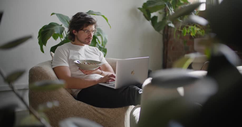 A male sitting on a chair is typing on a laptop