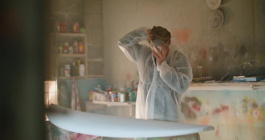 Man hangs up the phone and keeps working on a surfboard in a workshop