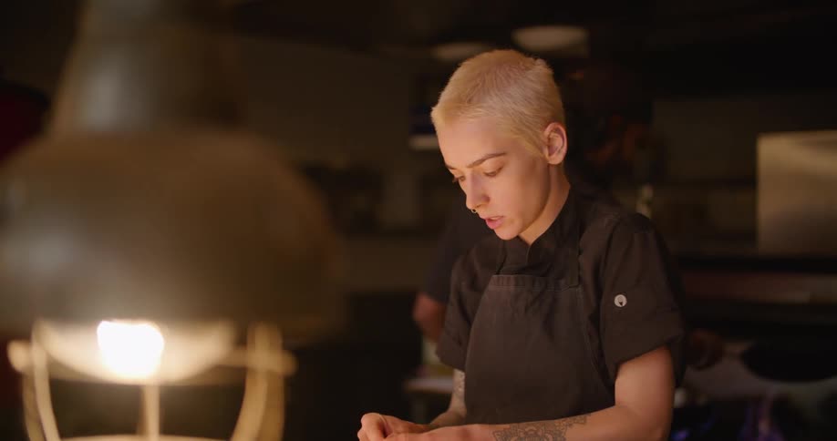A chef cutting onions in a restaurant kitchen talks to her colleague