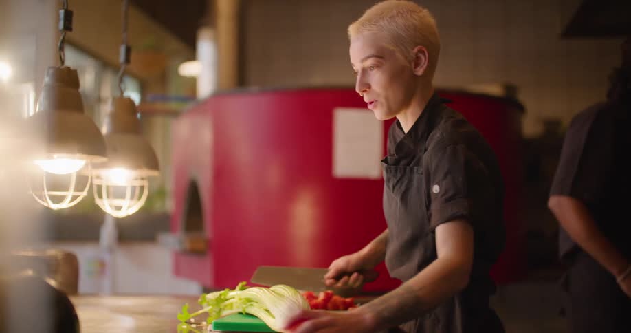 A woman in a kitchen cutting vegetables on a cutting board with a knife