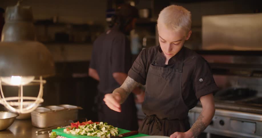 A chef sprinkles some seasoning on top of a raw steak in a restaurant kitchen
