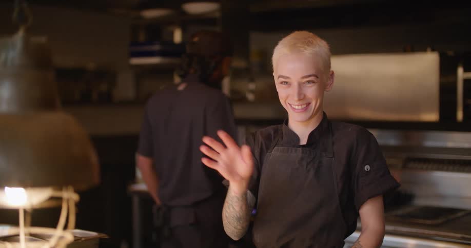 A restaurant chef stands in the kitchen speaking to another person