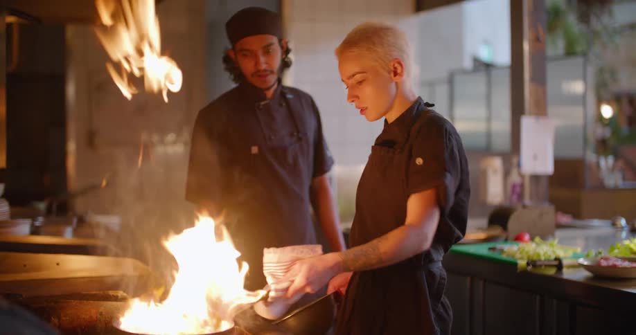 Chef flambeing food on a pan over a fire in a restaurant kitchen