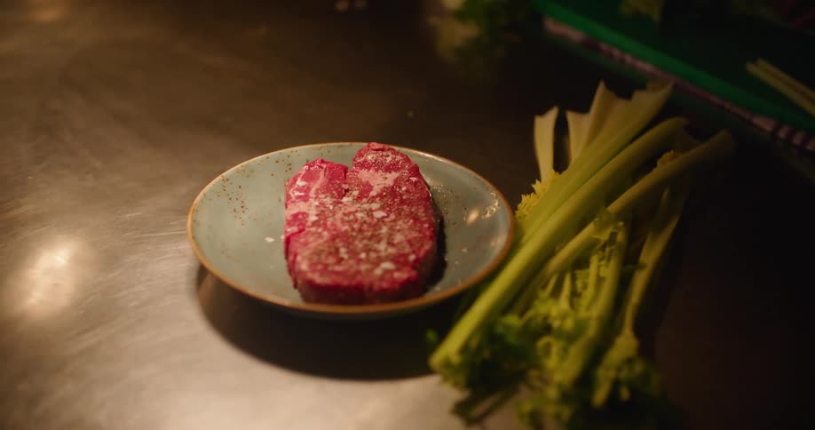 A raw steak with seasoning is passed on the table