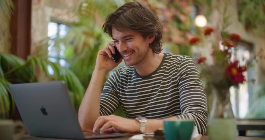 A man is talking on his cell phone while using a laptop