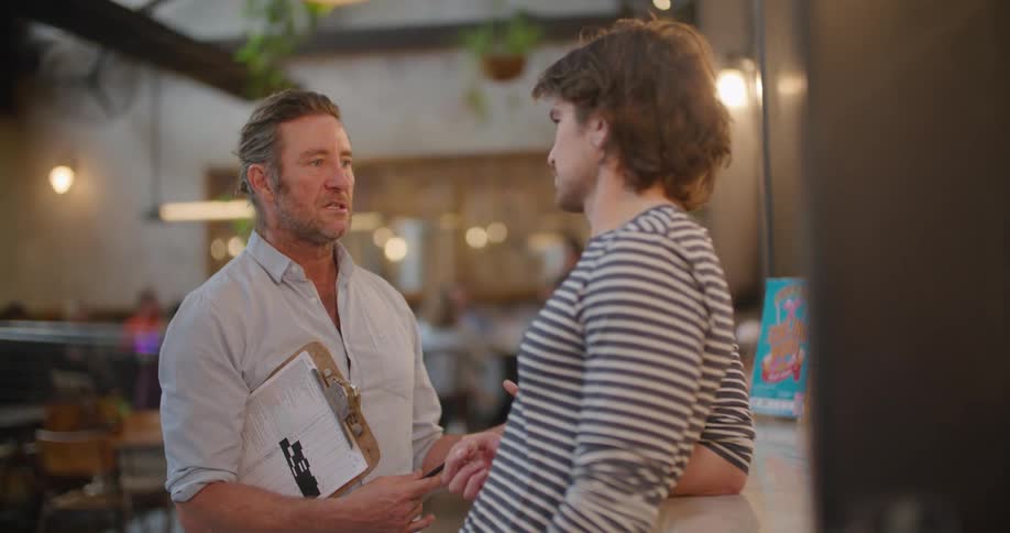 A restaurant manager speaks with an employee as they stand near the bar