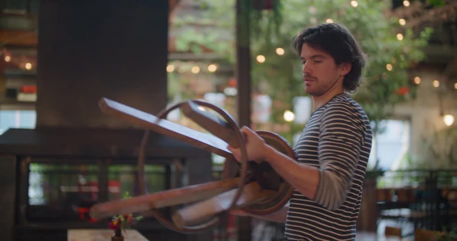 A restaurant employee moving stools from a tabletop before opening