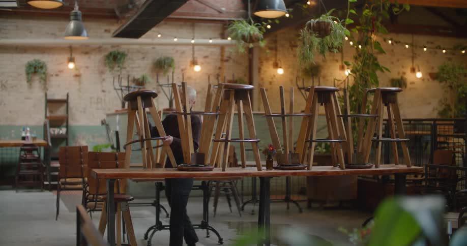 A restaurant worker moving stools from a tabletop before opening